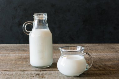 Koyu bir arka plan üzerinde ahşap bir masa üzerinde süt ve bir bardak süt bir şişe