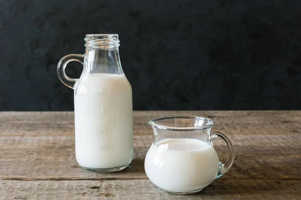 A bottle of milk and glass of milk on a wooden table on a dark background
