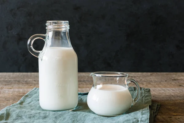 A bottle of milk and glass of milk on a wooden table on a dark background