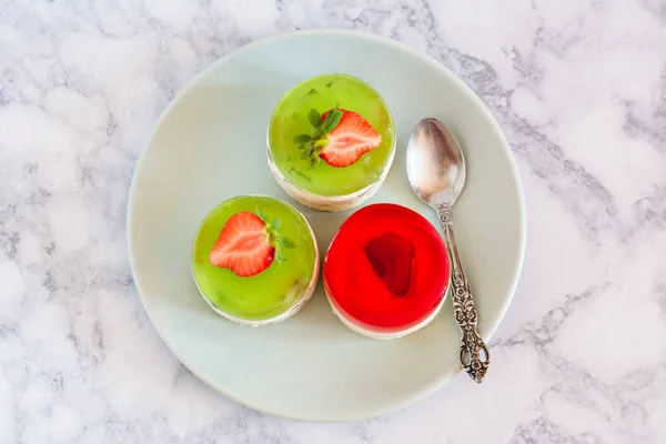 Mini round cold cheesecakes with fruit jelly and strawberries.