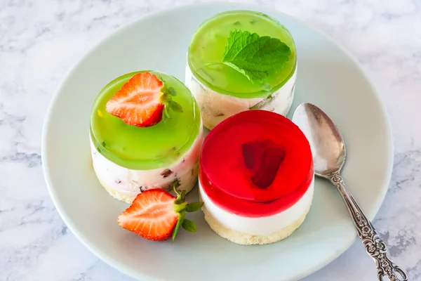 Mini round cold cheesecakes with fruit jelly and strawberries.