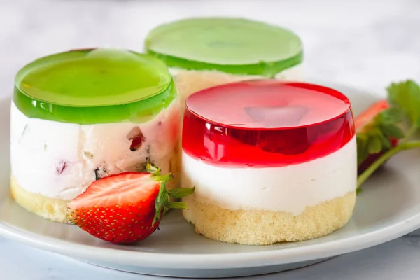 Mini round cold cheesecakes with fruit jelly and strawberries.