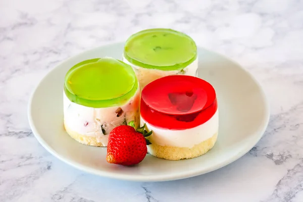 Mini round cold cheesecakes with fruit jelly and strawberries.