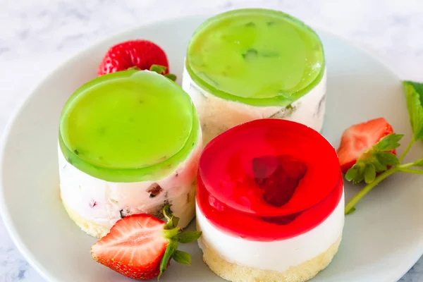 Mini round cold cheesecakes with fruit jelly and strawberries.