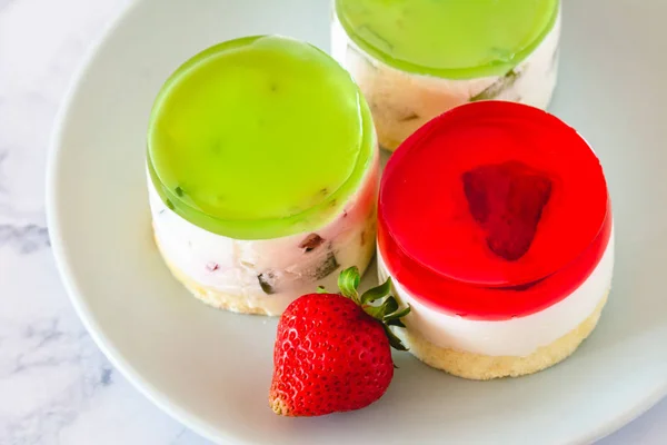 Mini round cold cheesecakes with fruit jelly and strawberries.