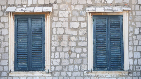 Two windows in old wall with closed blue shutters