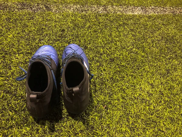 Black and blue football shoes on artificial grass