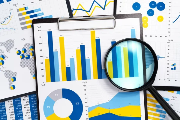 Analyzing marketing reports. Gathering statistical data.Pile of reports. Many charts and magnifying glass