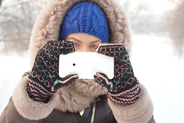 Young woman wearing warm clothes taking photos on mobile phone, frosty scene