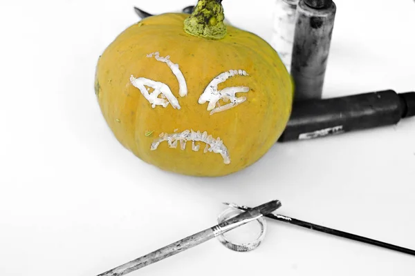 Selective color image of a painted halloween pumpkin on a table with brushes and colors around