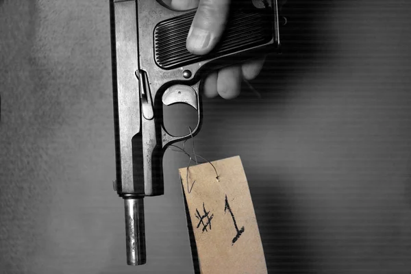 Human hand carefully holding a handgun tagged as a evidence, closeup studio shot