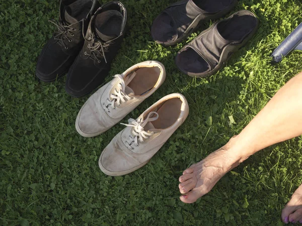 Bare female feet resting on the grass next to various shoes