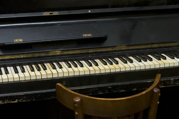 Old piano and a chair in front of it, indoor close-up