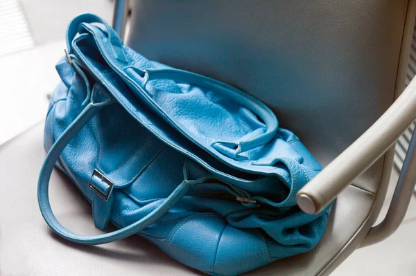 Blue leather lady handbag placed on a chair, indoor closeup