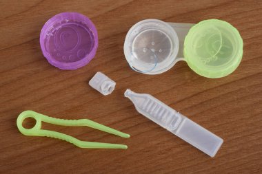 Kontakt lensler ve yapay gözyaşı göz damlası cımbız ve dava bir ahşap arka plan üzerinde