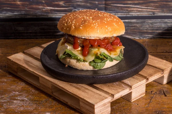 hamburger with cheese and ketchup on black wooden plate