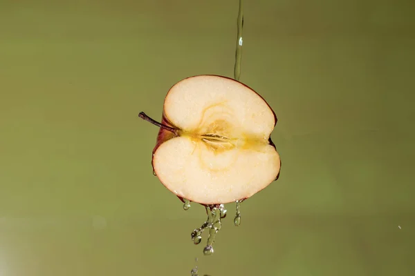 apple cut in different shapes with green background and splash of apple juice