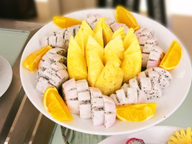 Dilimlenmiş tropikal meyveler masanın üstünde, en üstte. 