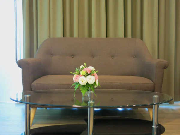 cozy brown sofa and flowers in vase on glass table in luxury interior
