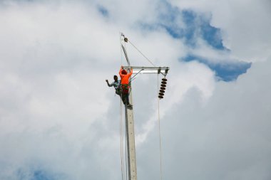 Mavi gökyüzü arka planına sahip elektrik direğinde inşaat işçisi.