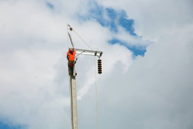 Mavi gökyüzü arka planına sahip elektrik direğinde inşaat işçisi.