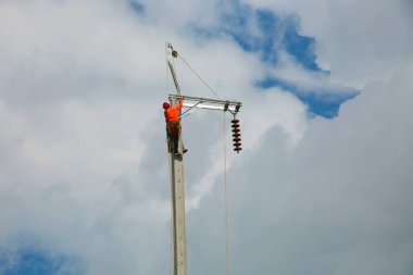 Mavi gökyüzü arka planına sahip elektrik direğinde inşaat işçisi.