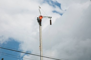 Mavi gökyüzü arka planına sahip elektrik direğinde inşaat işçisi.