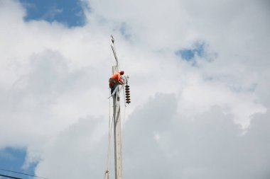 Mavi gökyüzü arka planına sahip elektrik direğinde inşaat işçisi.