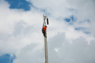 Mavi gökyüzü arka planına sahip elektrik direğinde inşaat işçisi.