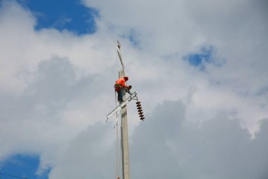 Mavi gökyüzü arka planına sahip elektrik direğinde inşaat işçisi.