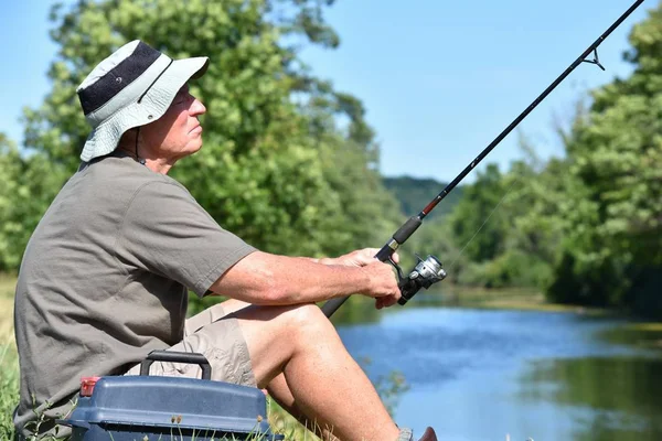 Senior männlicher Fischer sitzt mit Rute und Rolle im Freien — Stockfoto