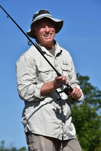 Sorrindo mais velho masculino pescador com haste e carretel ao ar livre — Fotografia de Stock