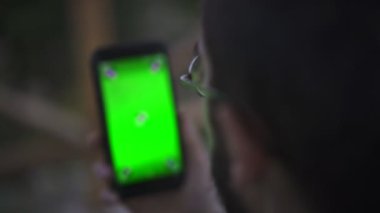 Genç adam tutarak Smartphone ile boş yeşil perde, açık havada  