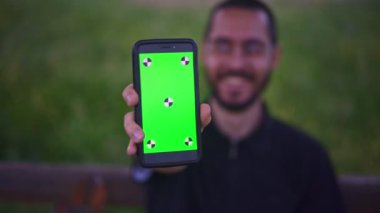 Genç adam tutarak Smartphone ile boş yeşil perde, açık havada  