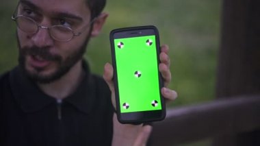 Genç adam tutarak Smartphone ile boş yeşil perde, açık havada  