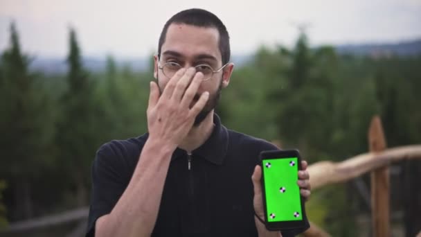 年轻男子手持智能手机与空绿色屏幕和微笑 — 图库视频影像