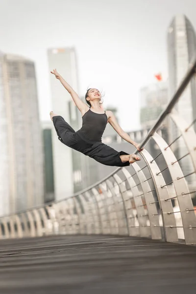 美丽的年轻女孩在城市跳舞 穿着黑色 与摩天大楼的背景 — 图库照片