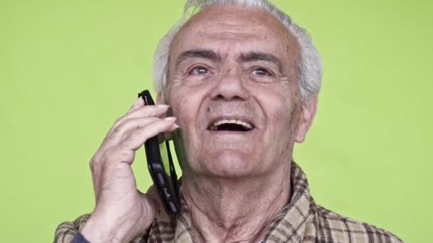 スマートフォンで話している高齢者の幸せな男は スローモーションビデオ 緑の背景をクローズアップ — ストック動画