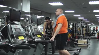 Belirleyici bir göz ile ayak üzerinde yürüyen şişman adam. Adamın yakışıklı genç çalıştırıcı onayladı, övgü, onu destekler. Sol taraftan görünüm