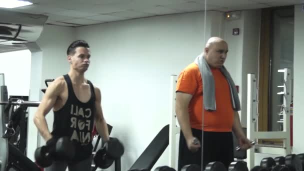 Fatty Man Picks Smallest Dumbbells Standing Next Handsome Athlete Picking — Stock Video