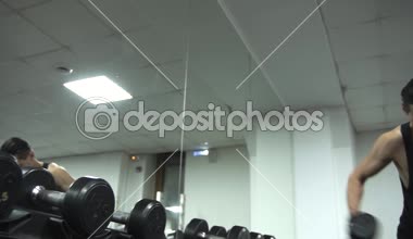 Şişko adam oturuyor ve tebessüm, eğlenceli video dumbbels ile güzel bir atlet arıyorsunuz. hareketli kamera