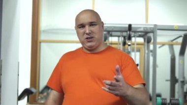 Turuncu şişman yakışıklı adam holding pırasa spor yapmak için motive t-shirt bir şey söyleyerek spor salonuna gitmek için çağırır. Sağlık motivasyon