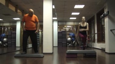 Şişman komik adam adımları yapmaya çalışıyorum. Genç güzel genç spor kadının yanına aktif step aerobik yapıyor