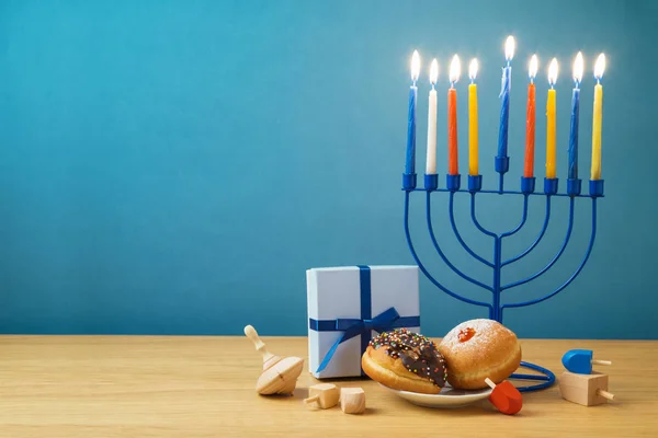 Jewish holiday Hanukkah background with menorah, sufganiyot, gift box and spinning tops on wooden table