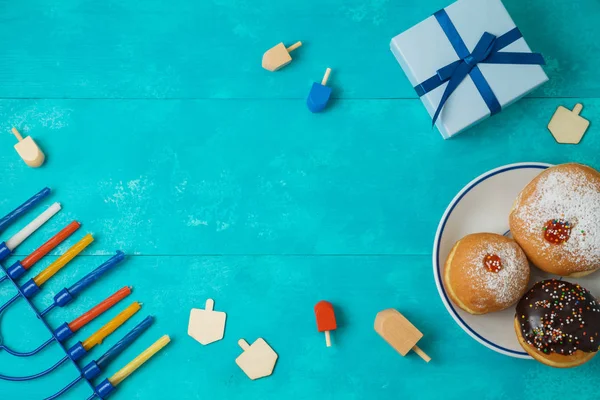 Jewish holiday Hanukkah concept with menorah, sufganiyot, gift box and spinning tops. Top view from above. Flat lay