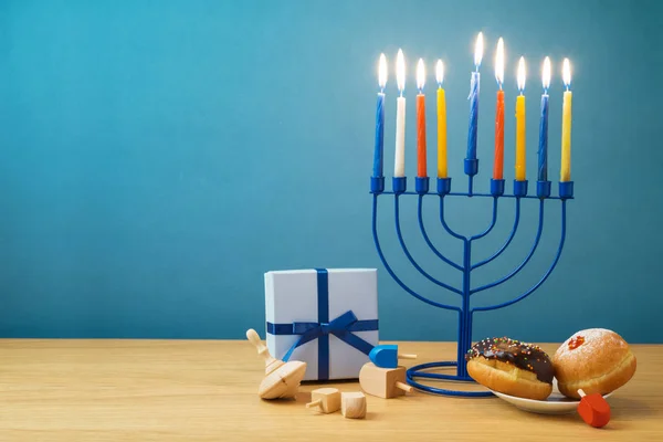 Jewish holiday Hanukkah background with menorah, sufganiyot, gift box and spinning tops on wooden table