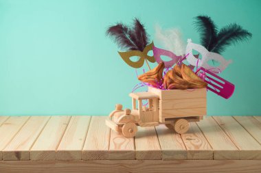 Yahudi tatil Purim arka plan ile oyuncak kamyon, karnaval maskesi, ahşap masa şenlikli ve hamantaschen çerezleri. Yaratıcı Purim sepet fikir