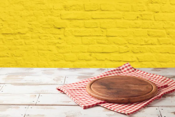 ピザ板と黄色のレンガ石の壁の背景にテーブル クロス空の木製テーブル 屋台に使用できます 主要視覚的なレイアウトや新しい製品の広告表示 — ストック写真
