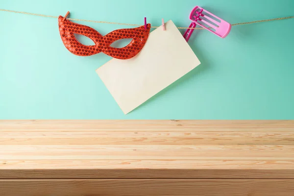 Jewish Holiday Purim holiday background with empty wooden table, paper note, carnival mask and noisemaker.