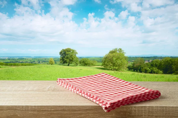 Empty wooden table with tablecloth over summer meadow background — Stock Photo, Image